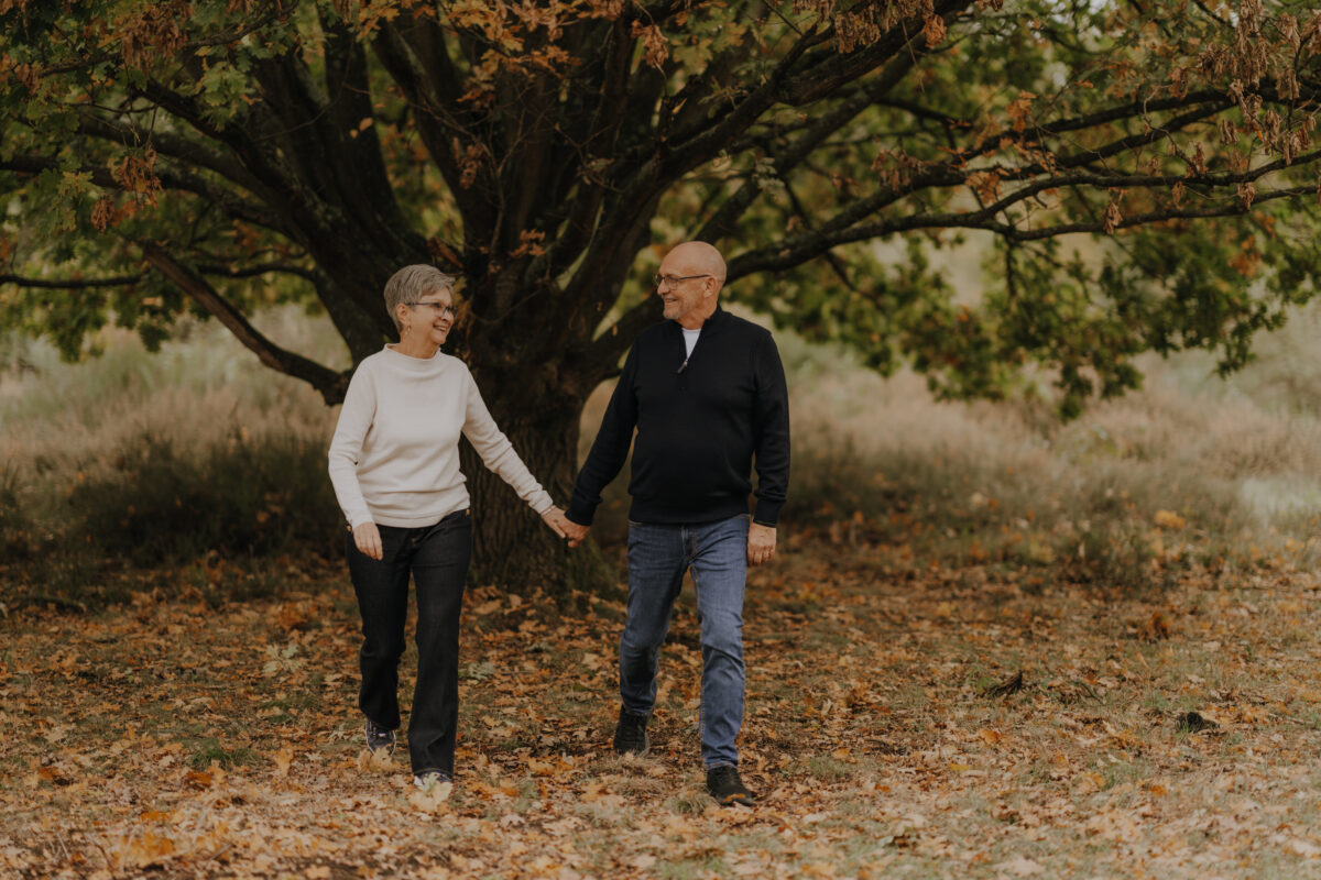 Paar schlendert Händchen haltend in einem Wald und schaut sich an