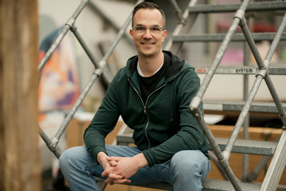 Portraitfoto eines Mannes, auf der Treppe sitzend, freundlicher Blick zur Kamera