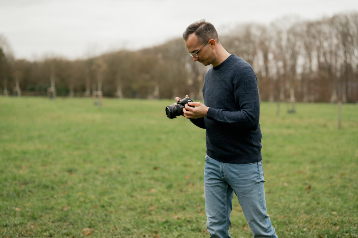 Portraitfoto eines Mannes mit Kamera in der Hand, auf einem Feld fotografiert