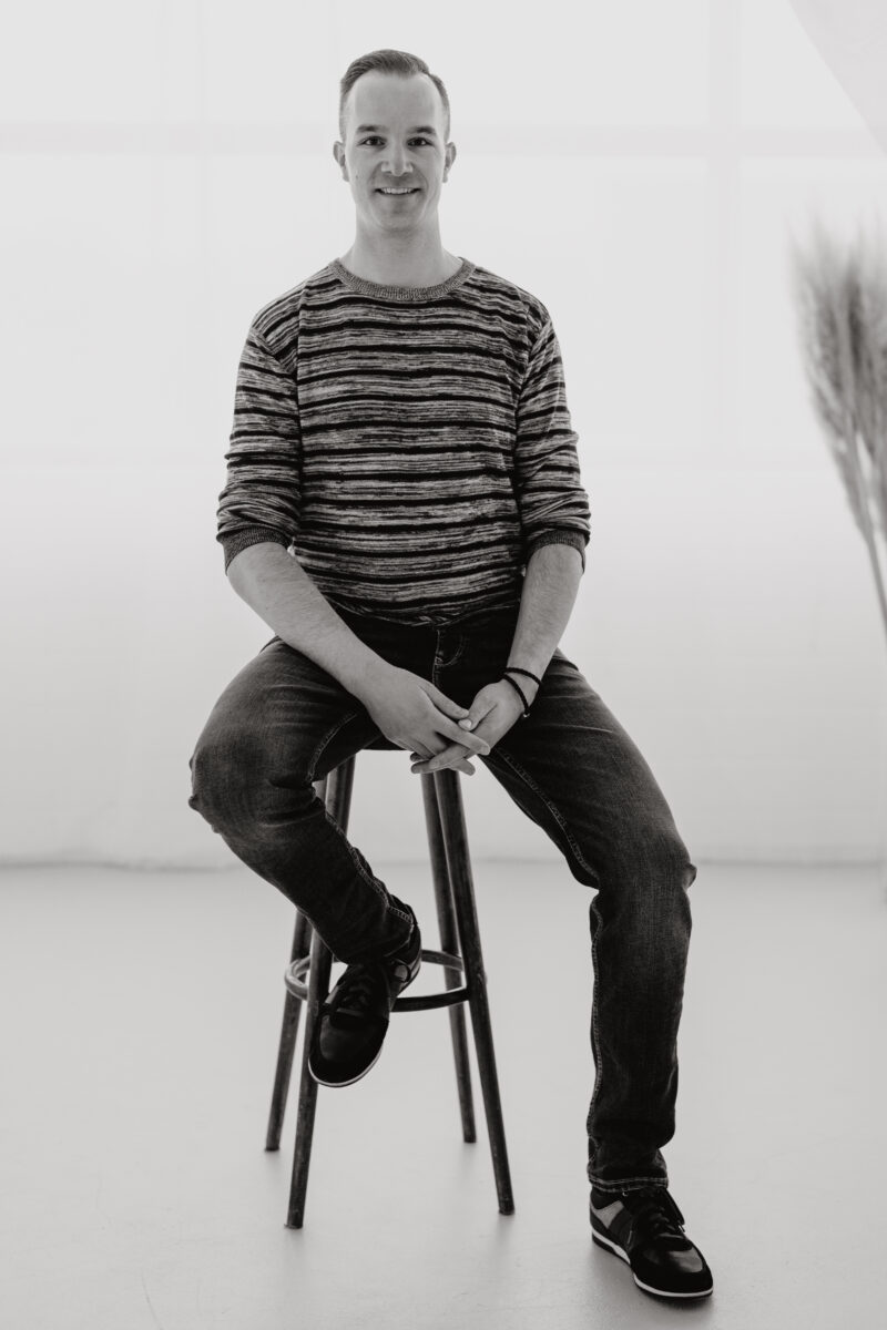 Schwarz-Weiß Portraitfoto eines Mannes sitzend auf einem Hocker