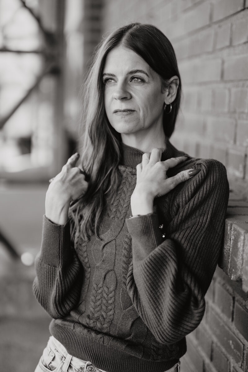 Schwarz-weiß Portraitfoto einer Frau, lehnt an einer Backsteinwand