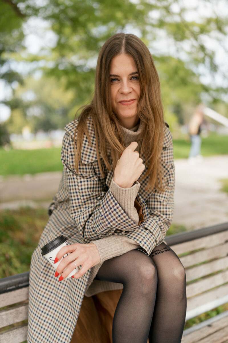 Portraitfoto einer Frau, auf einer Parkbank sitzend mit freundlichem Gesichtsausdruck