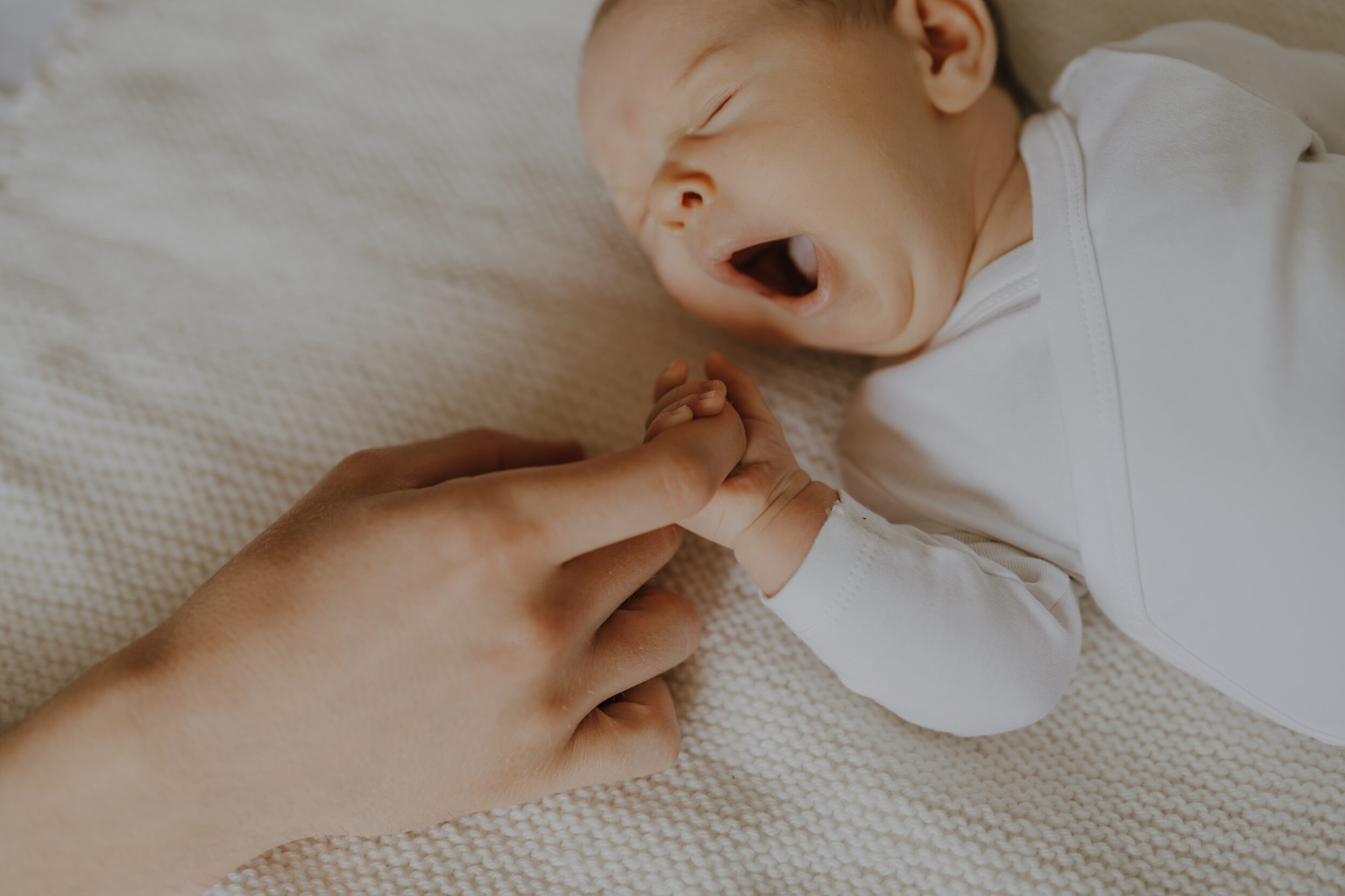 Newborn Portfolio Baby gähnt und hält Papas Finger im Händchen