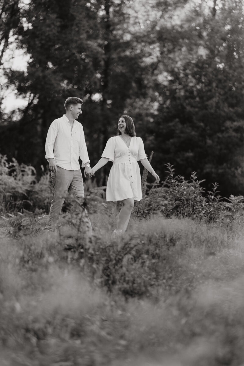 Paar geht Händchen haltend über eine Wiese und schaut sich an, fotografiert in Schwarz-Weiß