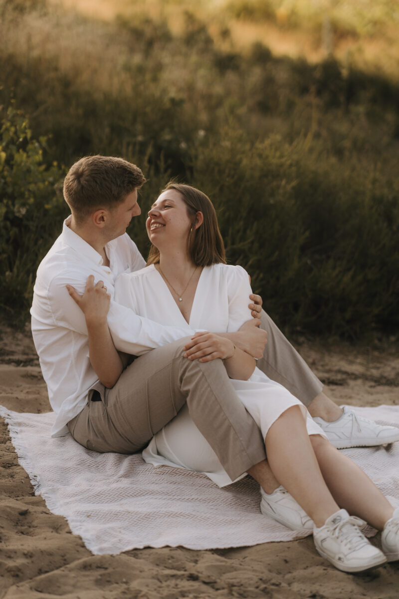 Paar sitzt Arm in Arm auf einer Decke und setzt zum Kuss an