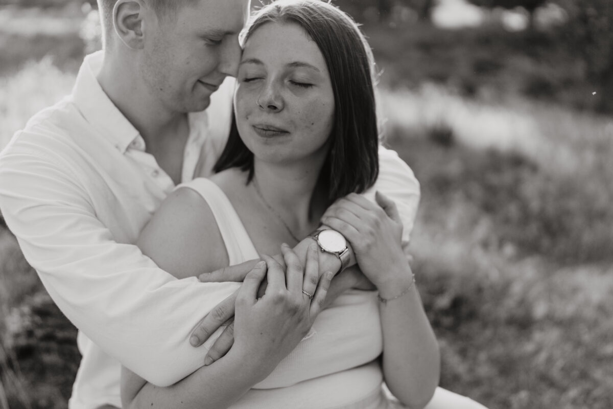 Er umarmt sie von hinten mit geschlossenen Augen, fotografiert in Schwarz-Weiß