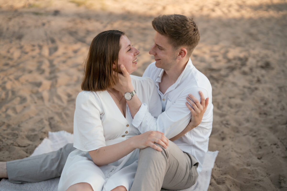 Paar sitzt Arm in Arm auf einer Decke und schaut sich in die Augen