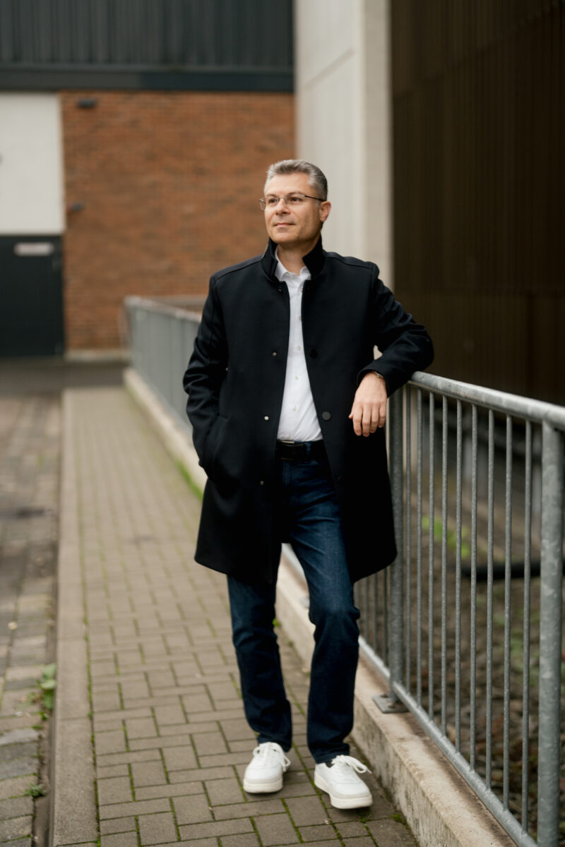 Portraitfoto eines Mannes, lehnt sich an ein Geländer an und lächelt