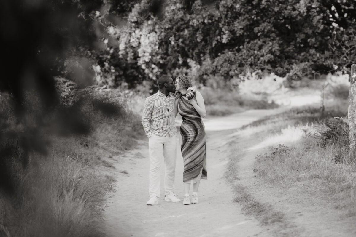 Paar läuft Arm in Arm auf die Kamera zu und küssen sich dabei, fotografiert in Schwarz-Weiß