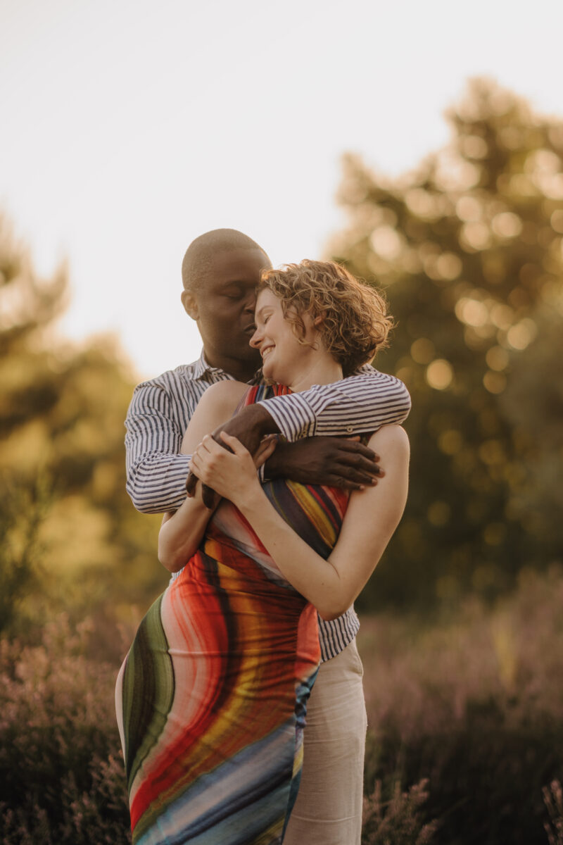 Er umarmt sie von hinten und sie lachen im Sonnenuntergang
