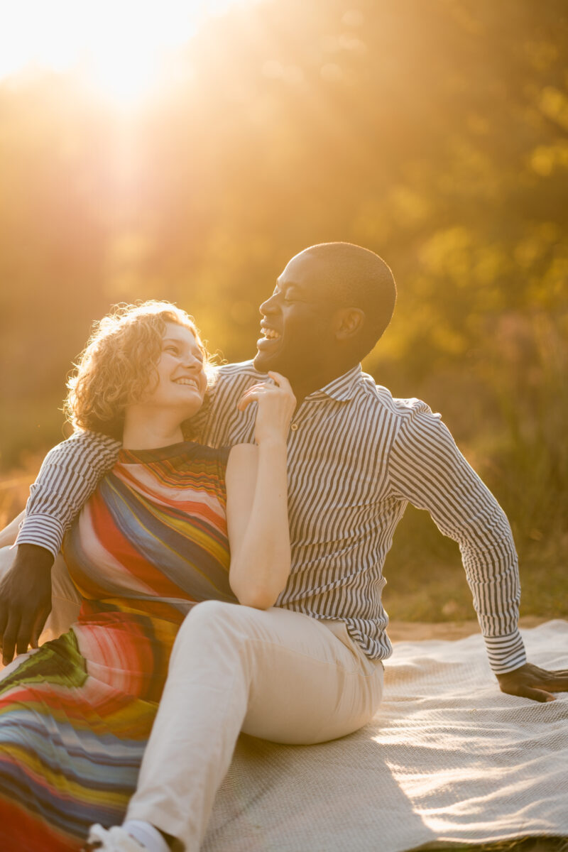Pärchen sitzt bei Sonnenuntergang zusammen auf einer Decke und lachen