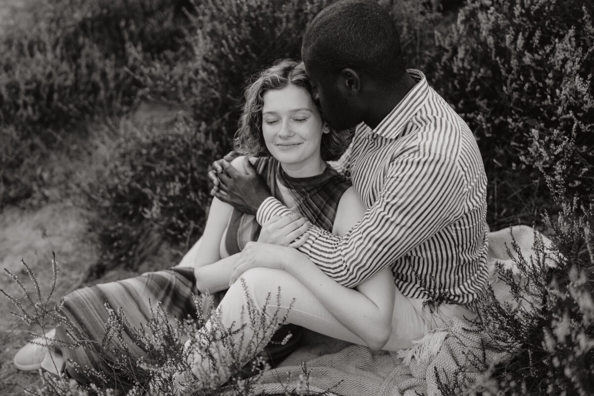 Paar liegt Arm in Arm auf einer Wiese und küssen sich, fotografiert in Schwarz-Weiß