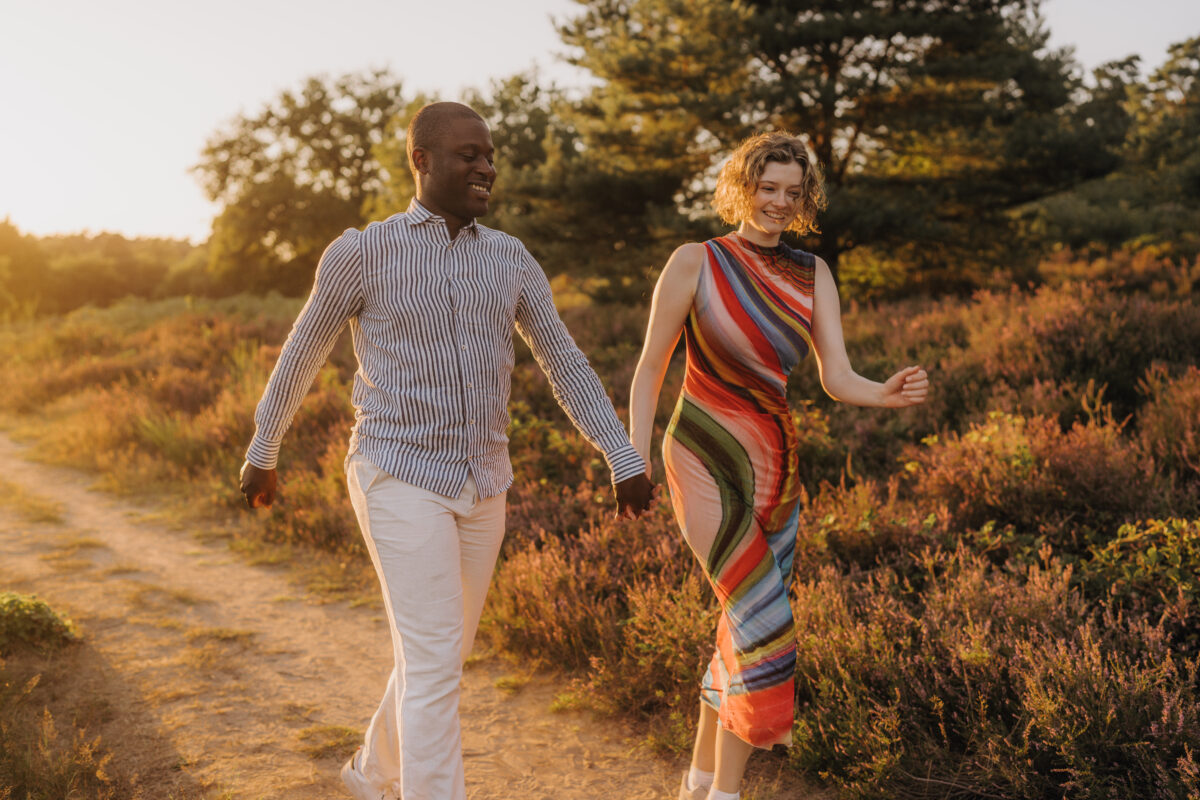 Paar läuft in der Abendsonne Händchen haltend über eine Wiese