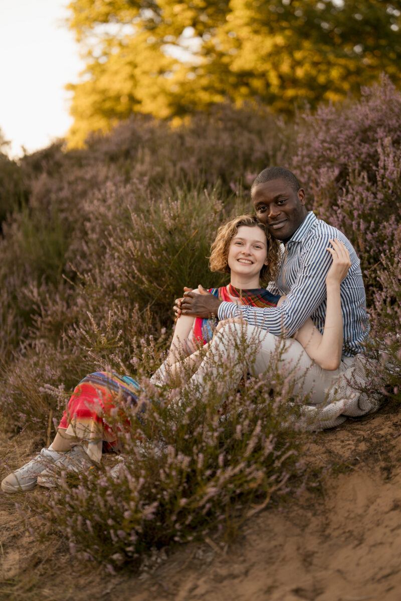 Paar sitzt Arm in Arm auf einer Wiese und schaut in die Kamera