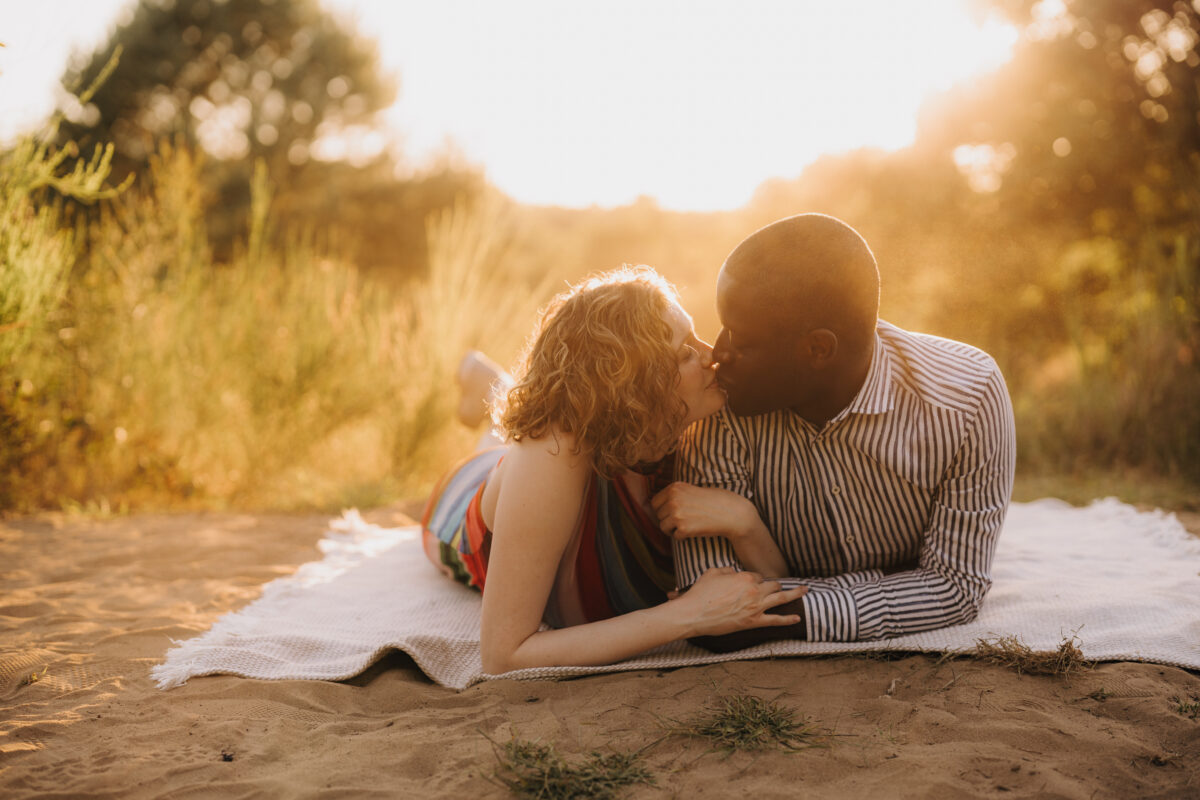 Paar liegt im Sonnenuntergang auf einer Decke und küsst sich