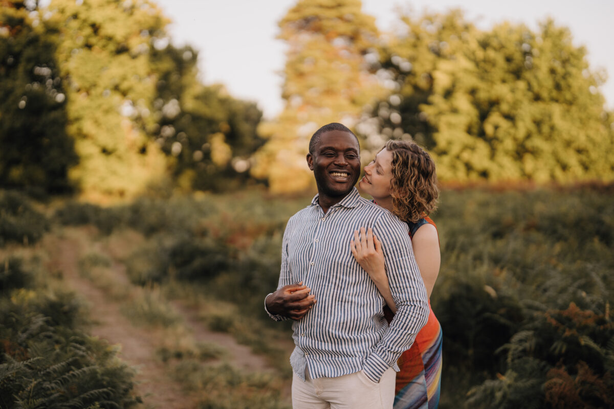 Frau umarmt Mann von hinten, beide Lächeln in der Natur