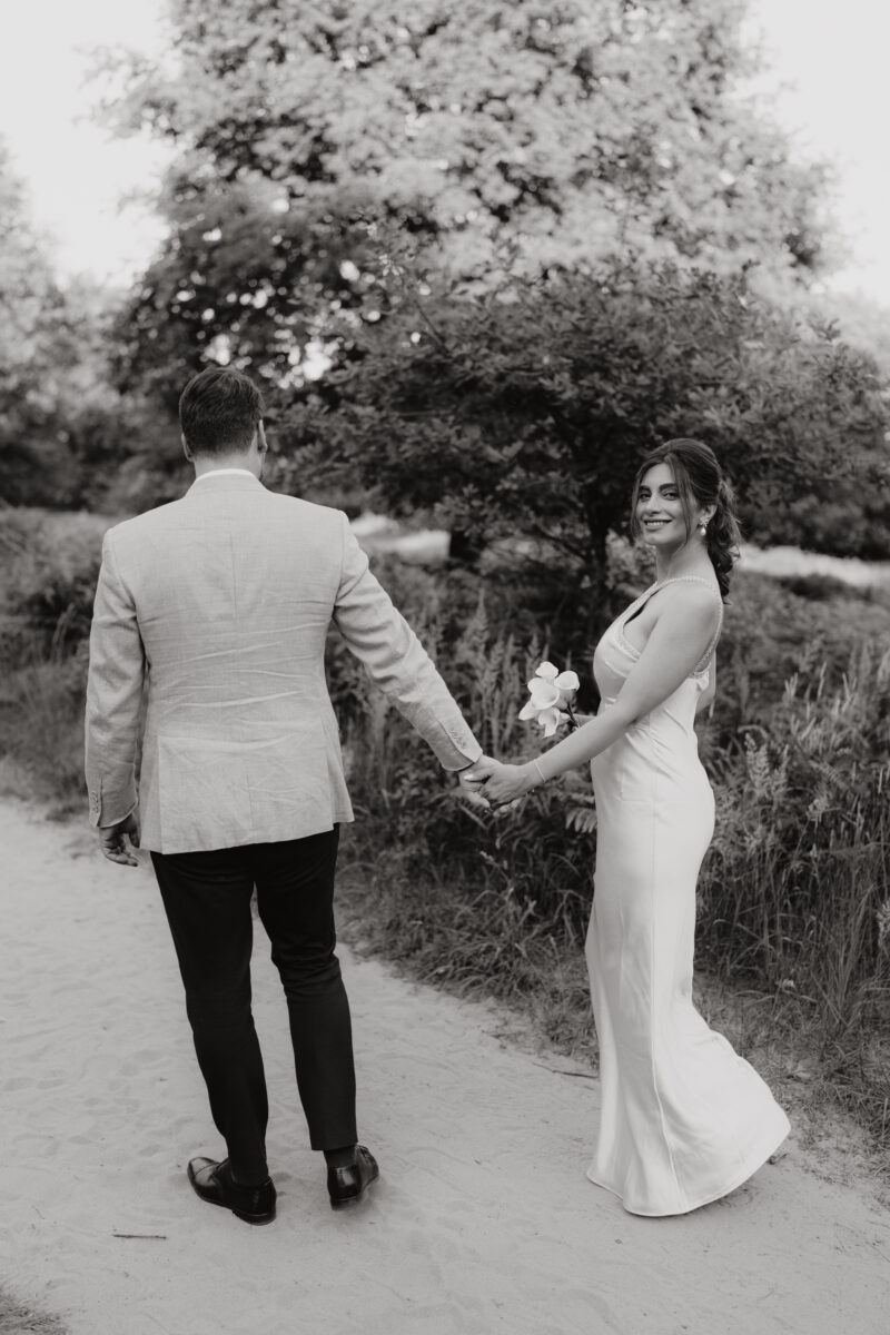 Paar schlendert Händchen haltend durch den Sand, sie schaut zurück in die Kamera, fotografiert in Schwarz-Weiß
