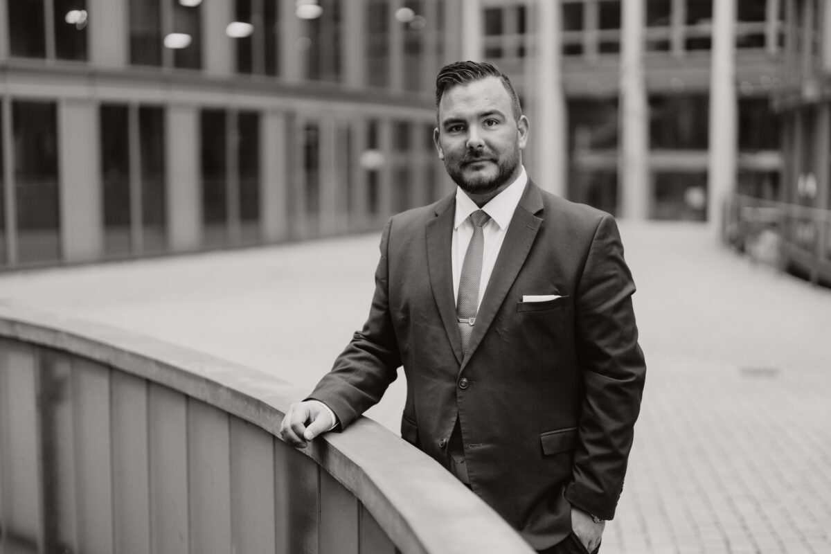 Schwarz-Weiß Portraitfoto eines Mannes wie er über ein Geländer lehnt