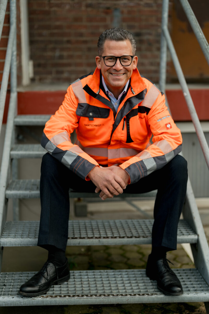 Portraitfoto eines Mannes sitzend auf einer Treppe in orangener Warnweste