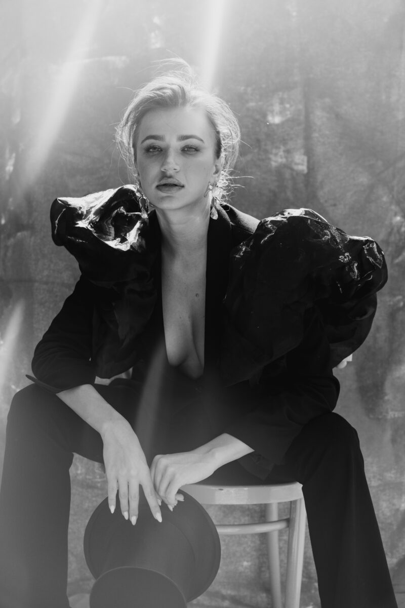 Schwarz-Weiß Portraitfoto einer Frau auf einem Stuhl sitzend, starker Blick in die Kamera