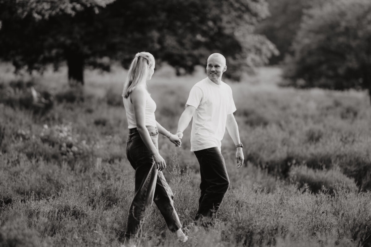 Paar schlendert Händchen haltend über eine Wiese und schaut sich an, fotografiert in Schwarz-Weiß