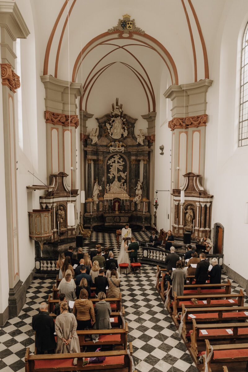 Hochzeitsportfolio, Aufnahme der Kirche mit dem Hochzeitspaar vorne und den Gästen