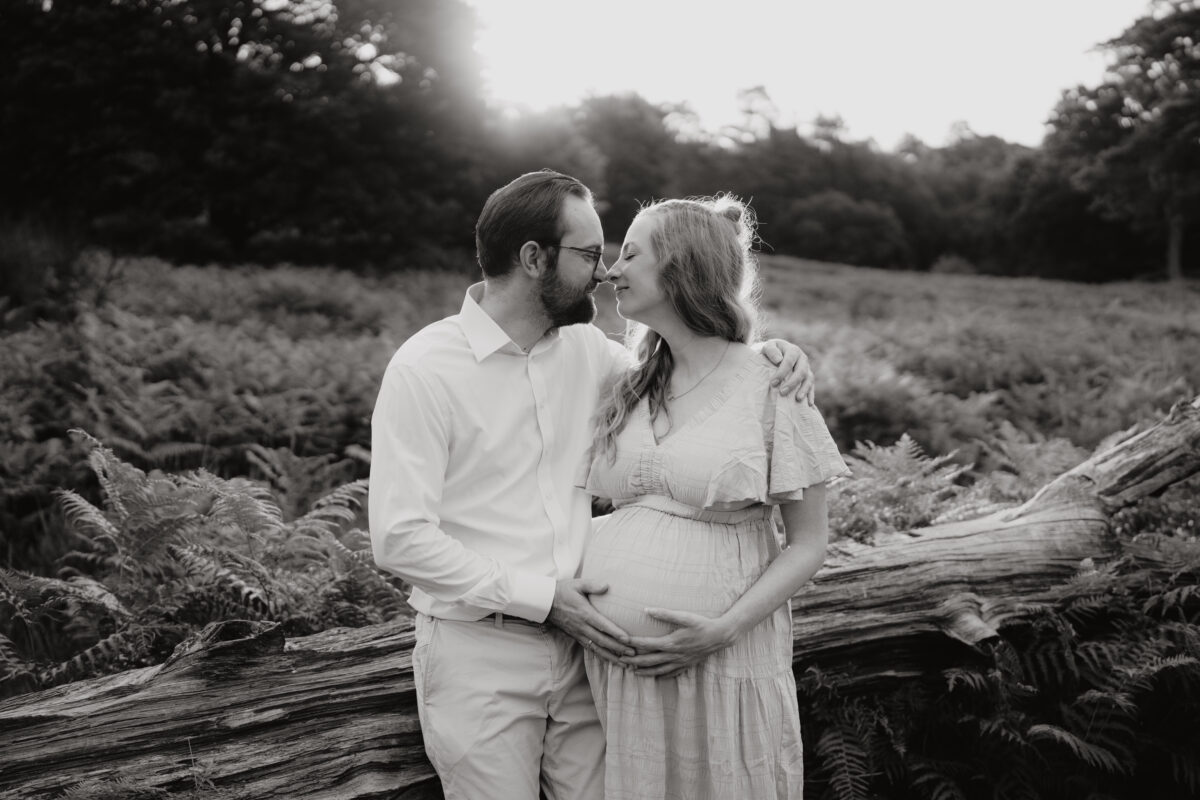 Babybauch Fotografie Portfolio glückliches junges Paar steht vor einer Wiese und schaut sich an Outdoor Schwarz-Weiß-Fotografie