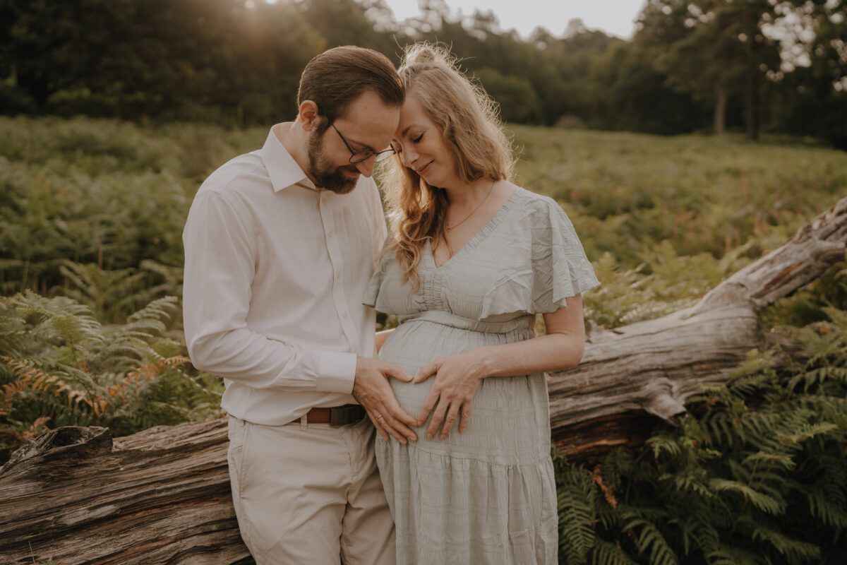Babybauch Fotografie Portfolio junges Paar formt mit den Händen ein Herz auf dem Babybauch in der Natur