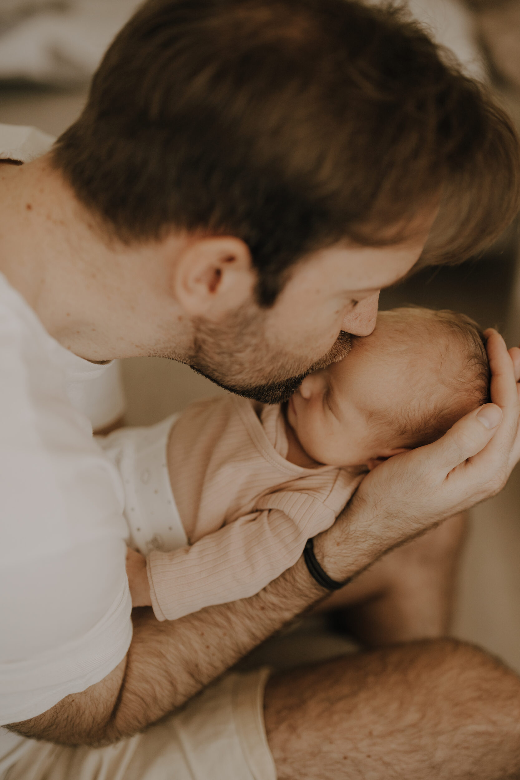 Newborn Portfolio Papa hält Baby in Beiden Armen/Händen und küsst es auf die Stirn