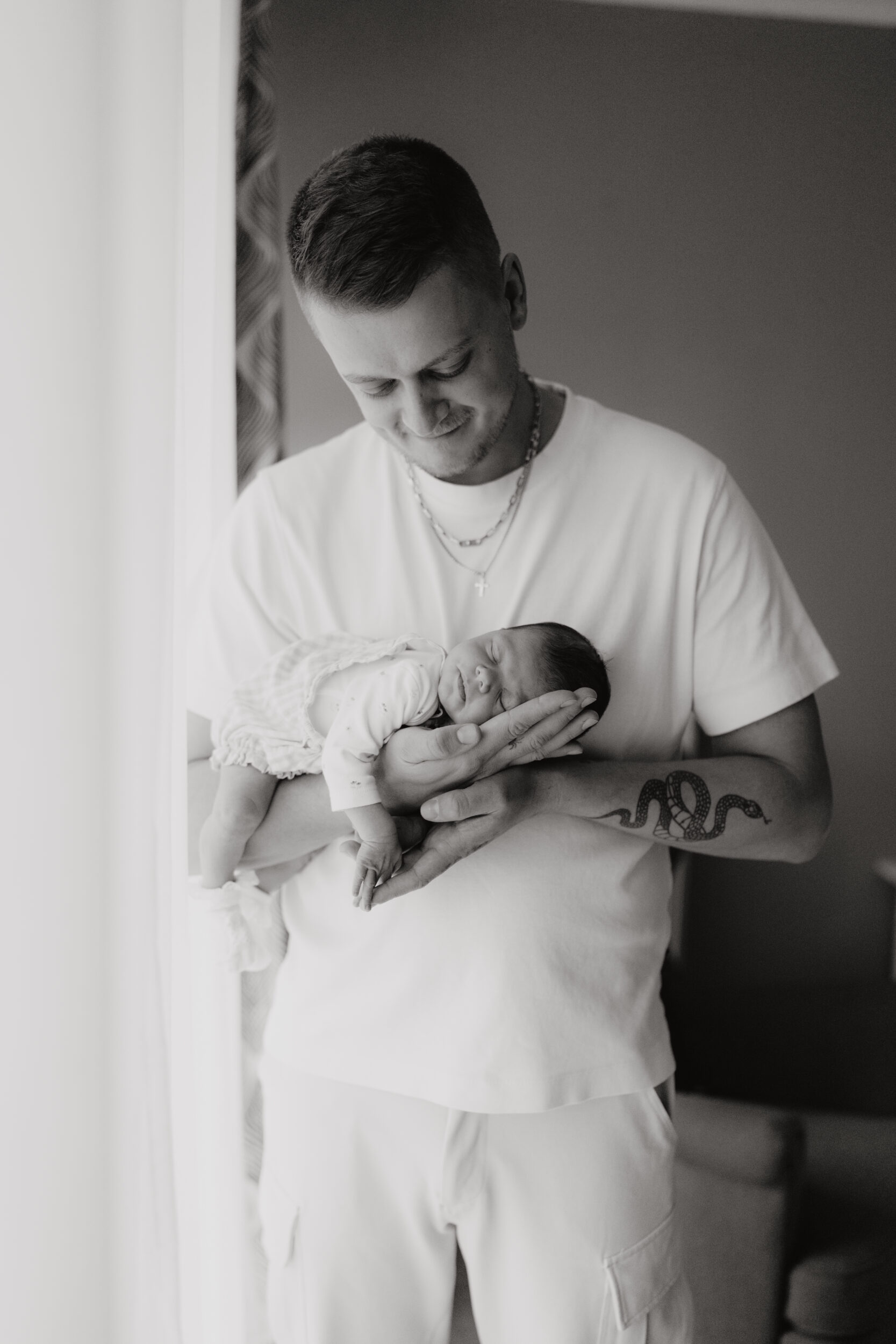 Newborn Portfolio Baby mit dem Bauch auf Papas Arm schwarz-weiß