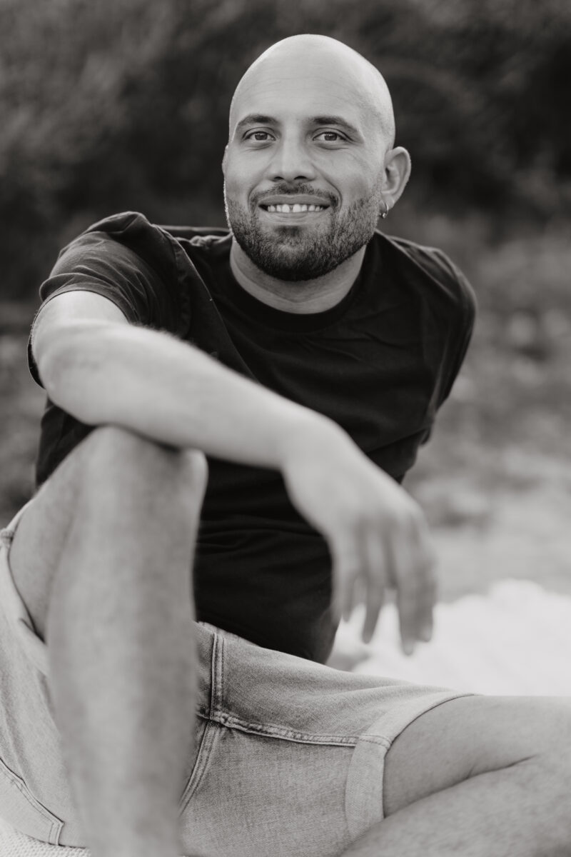 Schwarz-Weiß Portraitfoto eines Mannes, auf einer Picknickdecke sitzend und lächelnd