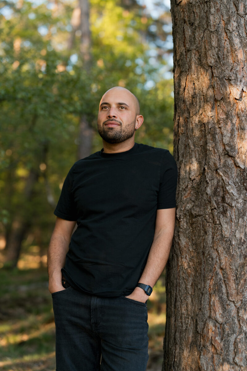 Portraitfoto eines Mannes an einen Baumstamm lehnend