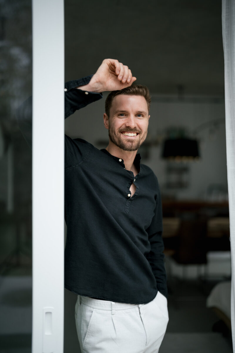 Portraitfoto eines Mannes, lächelnd und an einem Türrahmen lehnend