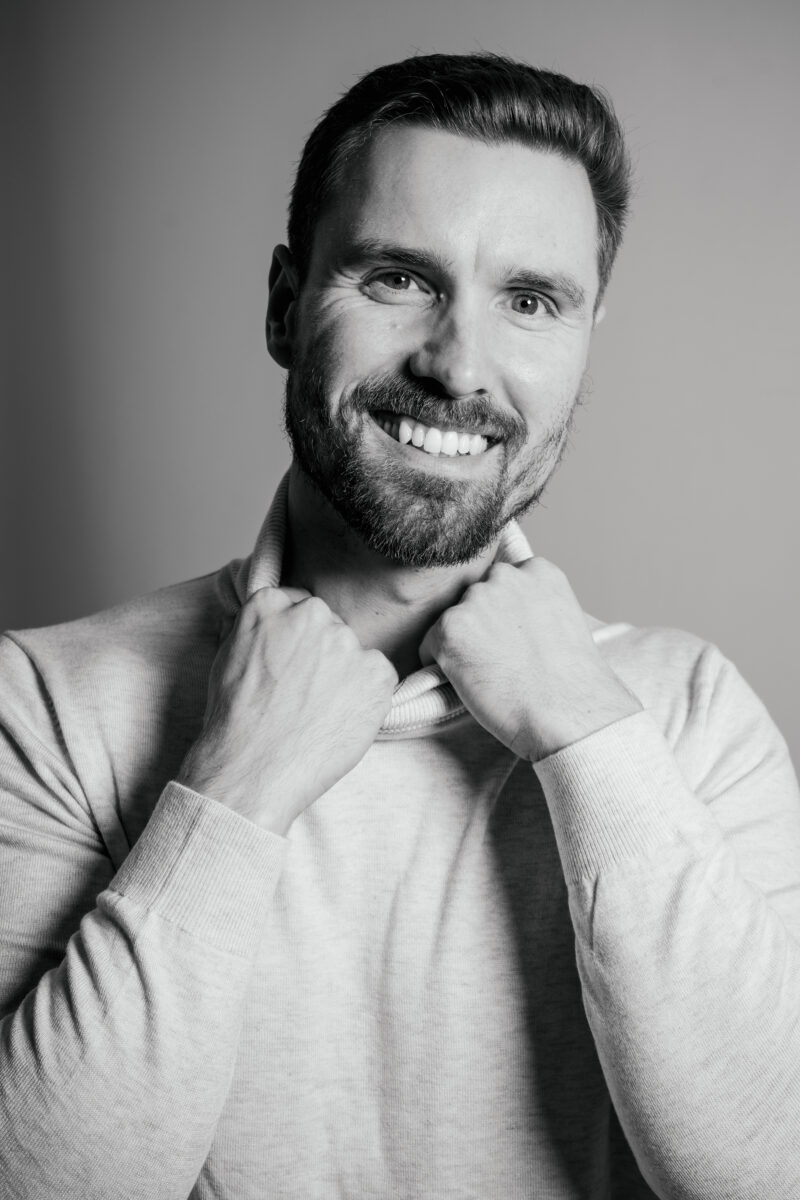 Schwarz-Weiß Portraitfoto eines Mannes, lächelnder Blick in die Kamera