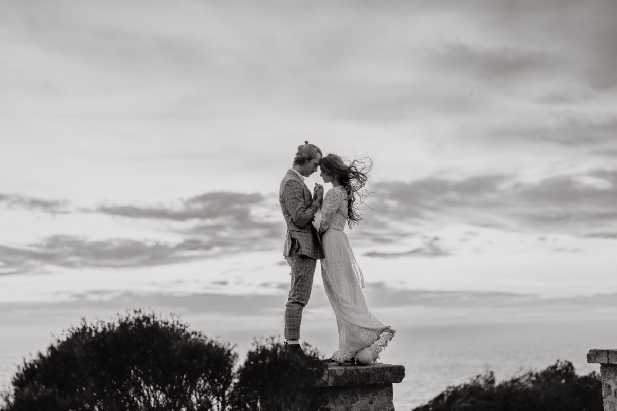 Hochzeitsportfolio, Braut und Bräutigam stehen nah beieinander, Kopf an Kopf auf einer erhöhung im Hintergrund das Meer und der Himmel