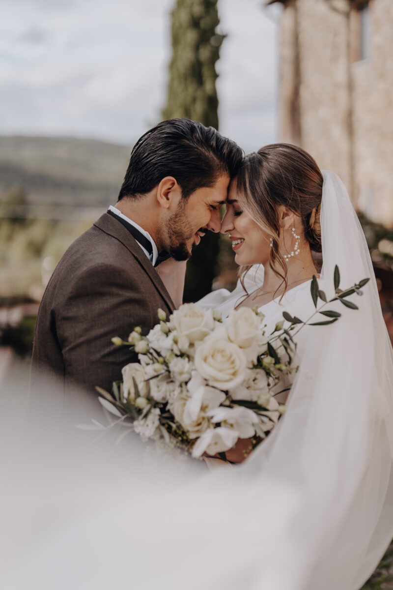 Destination Wedding Portfolio Hochzeitspaar Stirn an Stirn mit weißem Brautstrauß vor verschwommenem Hintergrund