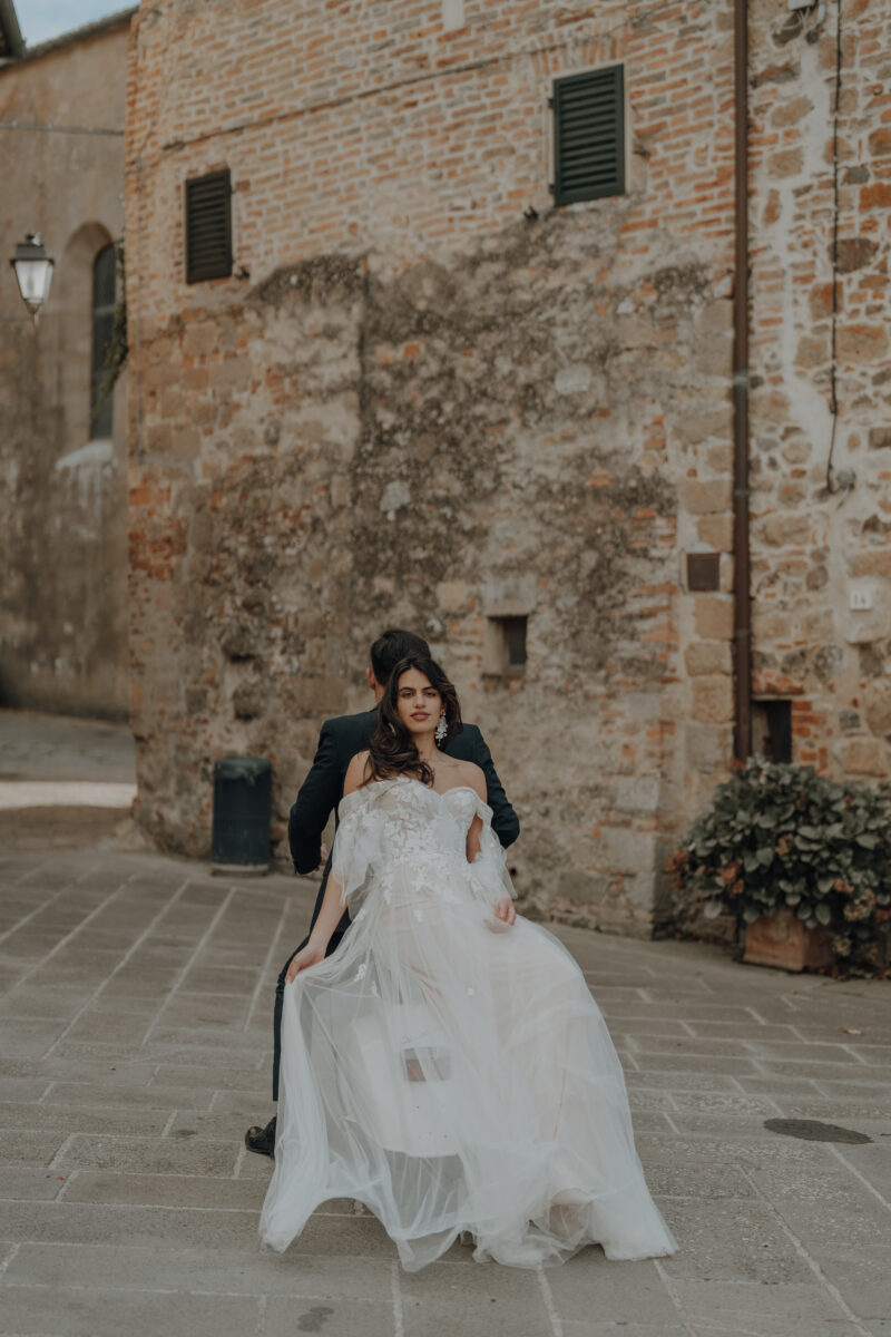 Destination Wedding Portfolio Hochzeitspaar steht Rücken an Rücken vor einem Haus, Braut im Vordergrund