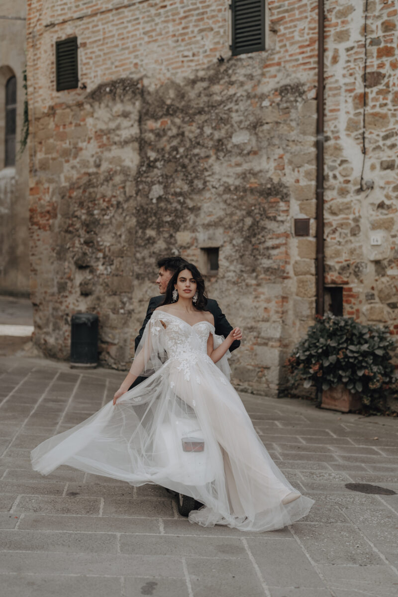 Destination Wedding Portfolio Hochzeitspaar steht Rücken an Rücken vor einem Haus, Braut im Vordergrund