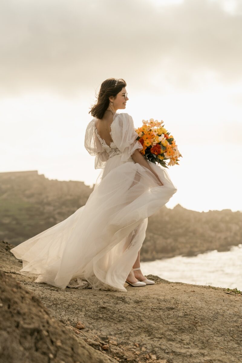 After Wedding Portfolio, Braut steht in der Mitte des Bildes vor einer Insellandschaft. Sie schaut nach rechts in die Ferne und hält ihren Blumenstrauß