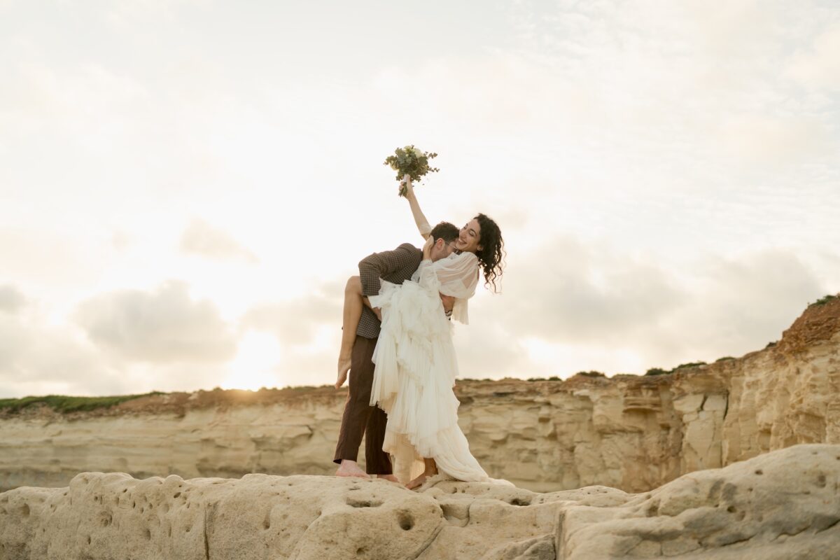 After Wedding Portfolio, Braut und Bräutigam stehen innerhalb einer Felsenlandschaft. Bräutigam hält das Bein und den Rücken der Braut umschlungen. Sie hält den Brautstrauß nach oben gerichtet und lacht