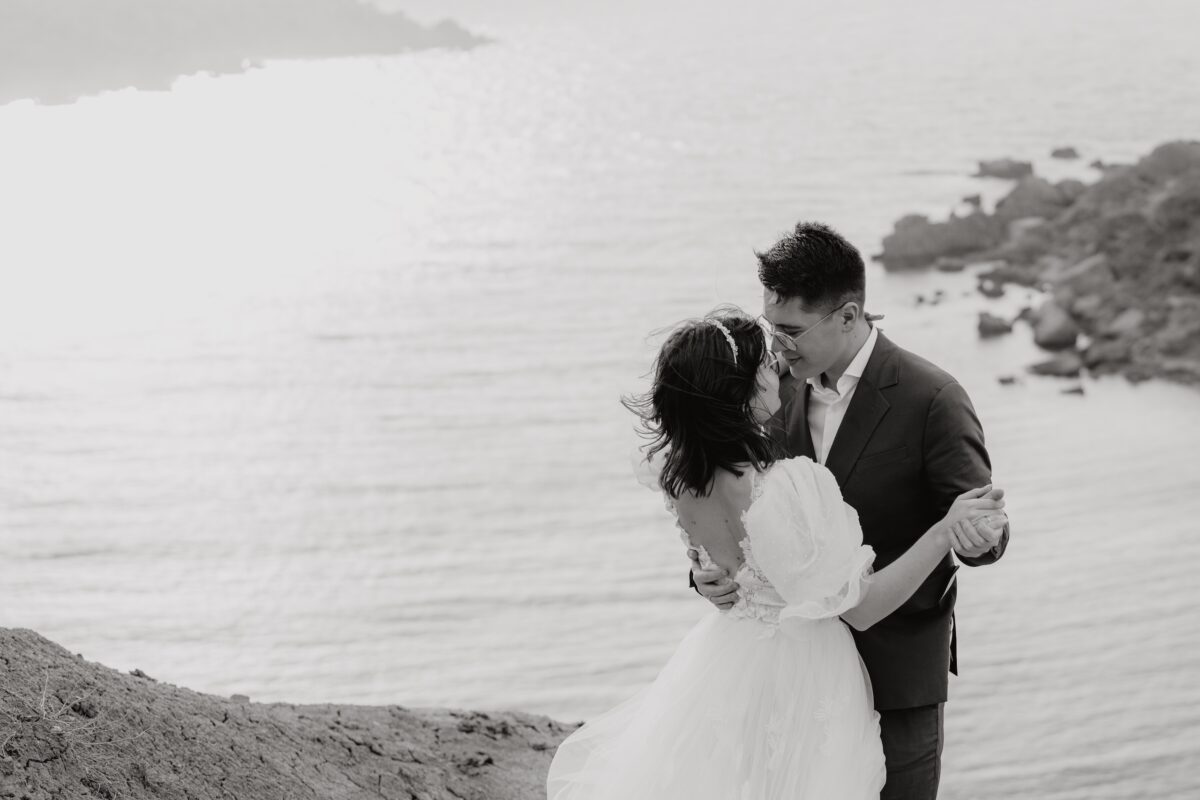 After Wedding, Braut und Bräutigam tanzen zusammen vor dem Meer und schauen sich verliebt in die Augen.