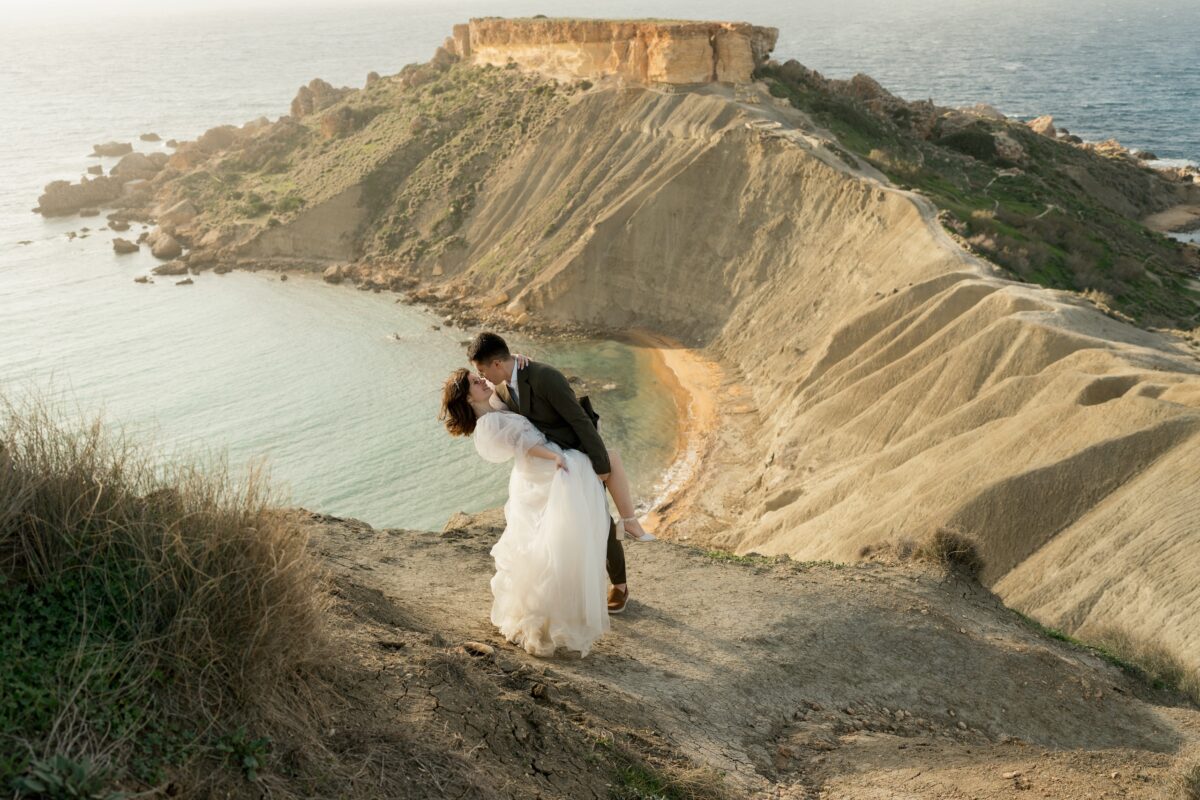 After Wedding, Braut und Bräutigam küssen sich vor einer Felsenlandschaft. Der Brautigam lehnt seine Braut nach hinten und hält ihr Bein fest.