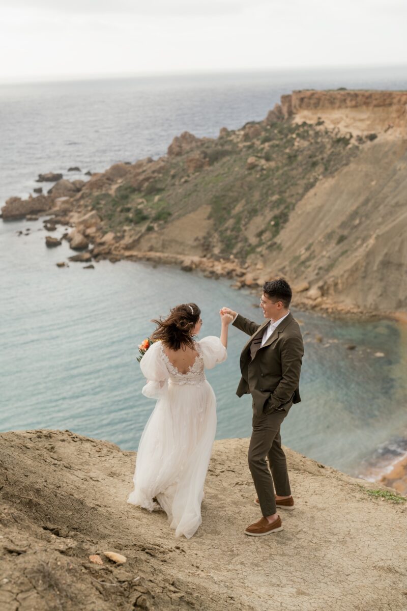 After Wedding Portfolio, Braut und Bräutigam stehen oben auf einem Felsen, im Hintergrund sieht man die Insellandschaft und das Meer. Sie halten sich an der Hand und schauen sich glücklich an.