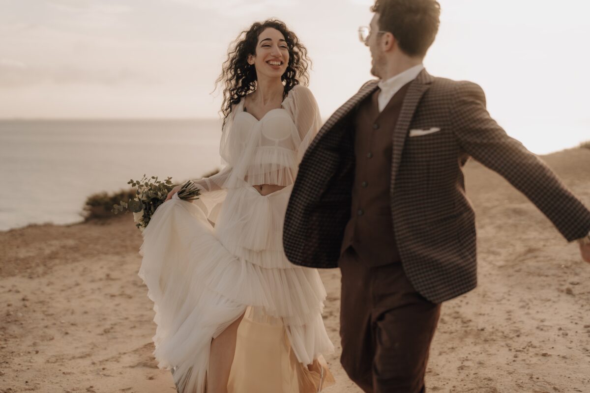 After Wedding, Braut und Bräutigam lachen sich beide an und laufen zsm nach vorne. Sie halten sich dabei an der Hand.