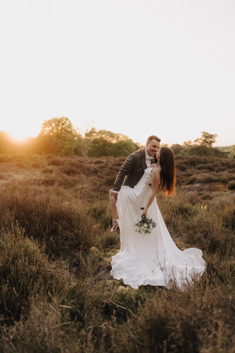 After Wedding Portfolio, Braut und Bräutigam befinden sich auf einer Heide. Er lehnt sie leicht nach hinten und hält ihr Bein fest. Beide schauen sich verliebt an.