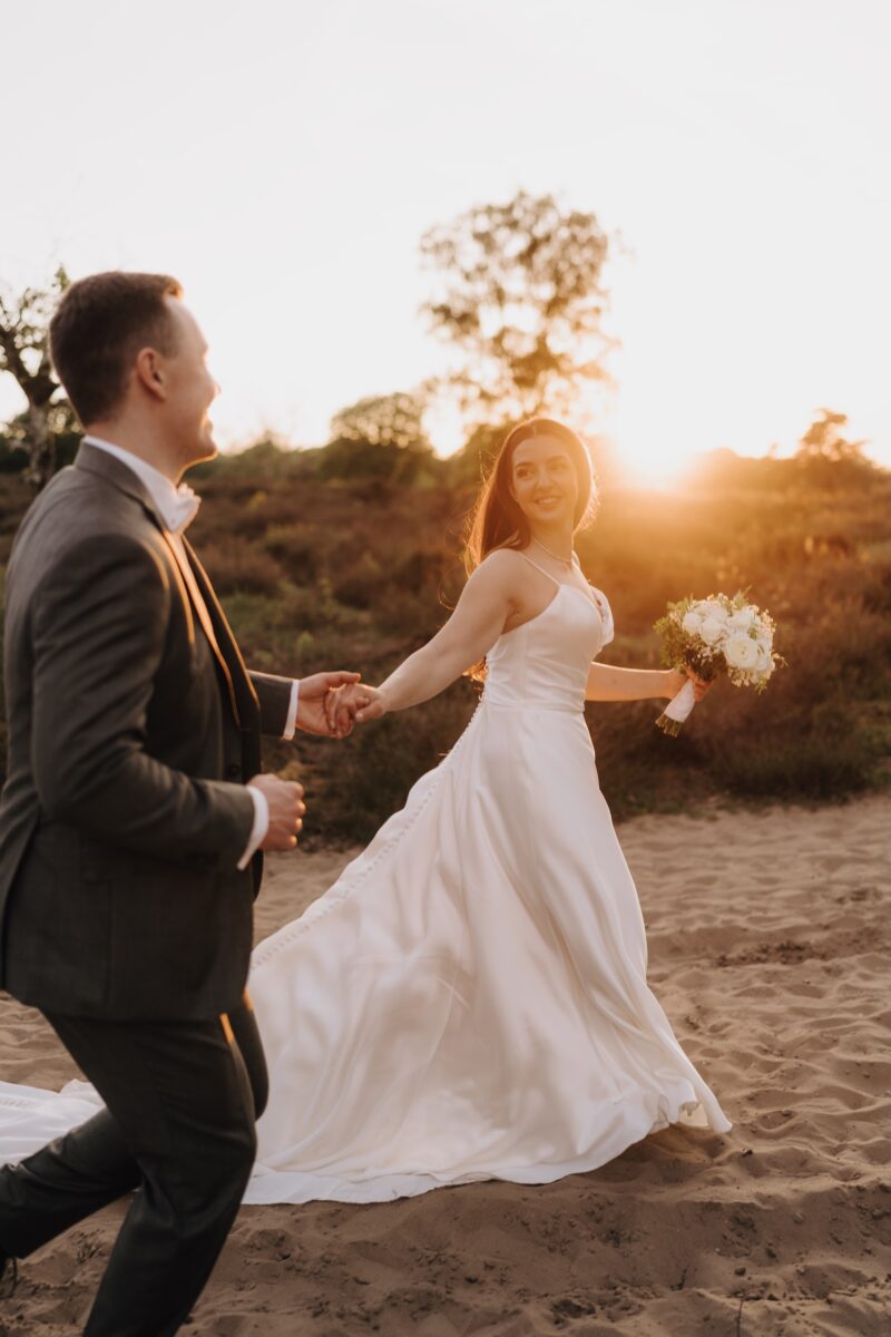 After Wedding Portfolio, Braut und Bräutigam halten sich an der Hand. Beide schauen sich glücklich an. Die Sonne strahlt sie traumhaft an