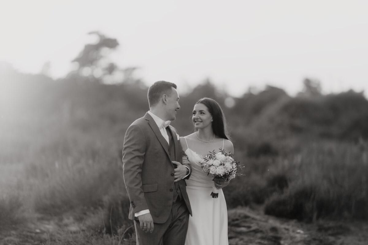 Hochzeitsportfolio, Braut und Bräutigam gegenseitig eingehackt. Sie schauen sich aneinander an und lächeln.