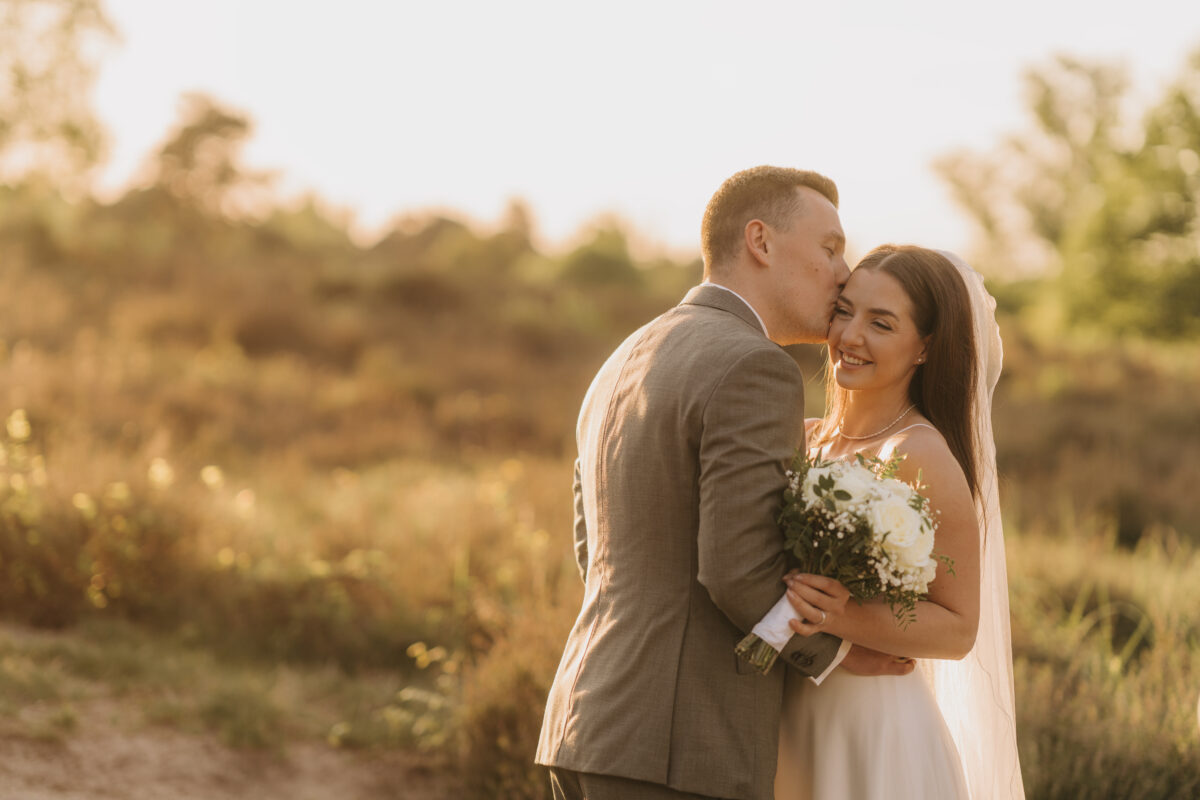 Hochzeitsportfolio, Romantisches Brautpaarshooting im Abendlicht in der Natur, Bräutigam nimmt die Braut in den Arm und gibt ihr einen Kuss auf die Schläfe | Hochzeitsfotografie Köln