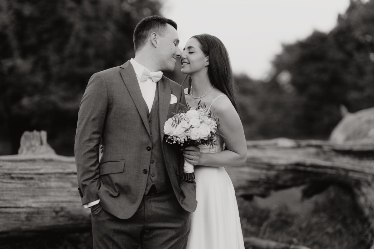 Hochzeitsportfolio, Braut und Bräutigam ganz nah aneinander. Ihre Nasenspitzen berühren sich. Sie ist bei ihm eingehackt und hält ihren Blumenstrauß