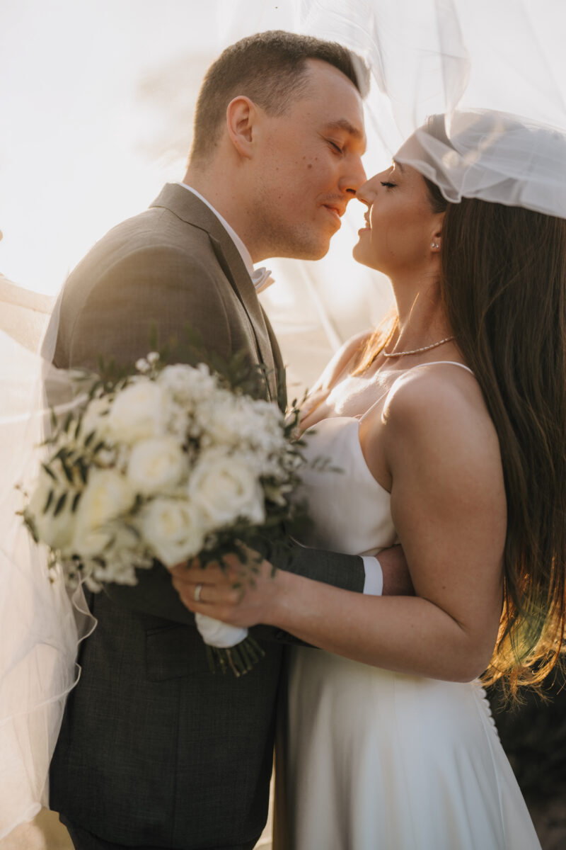 Hochzeitsportfolio, Romantisches Brautpaarporträt mit Brautstrauß im Abendlicht, der Schleier fliegt über beide und umhüllt sie | Hochzeitsfotografin Köln